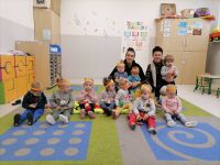 Dzieci siedzące na dywanie i pozujące do zdjęcia z dwiema opiekunkami